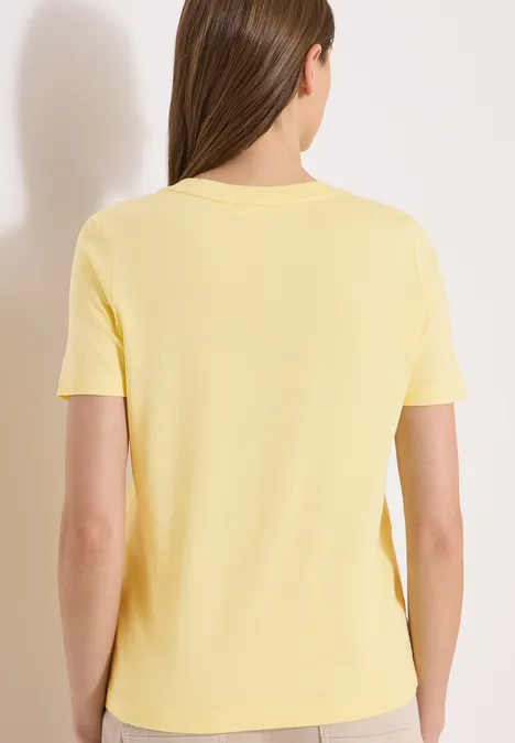 Rugaanzicht van een vrouw in een geel T-shirt met korte mouwen voor een neutrale achtergrond.