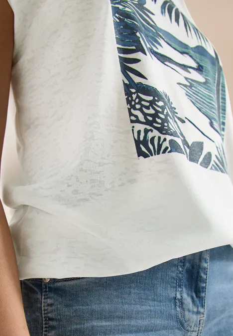 Seitliche Ansicht einer Person mit weißem Shirt mit Tropen-Print und blauen Jeans.