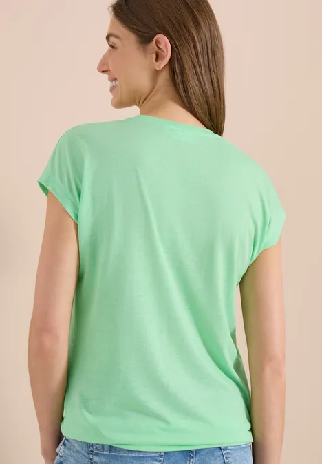 Frau von hinten mit mintgrünem T-Shirt und kurzen Ärmeln, vor neutralem Hintergrund.