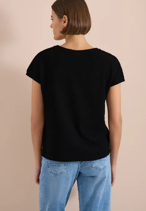 Frau von hinten in schwarzem T-Shirt und hellblauen Jeans vor beigefarbenem Hintergrund.