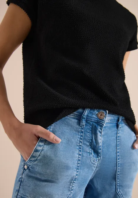 Schwarzes Strickshirt, hellblaue Jeans, Hände in den Taschen.