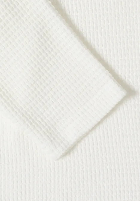 Gros plan sur un tissu blanc à structure gaufrée, motif nid d’abeille ou losanges.