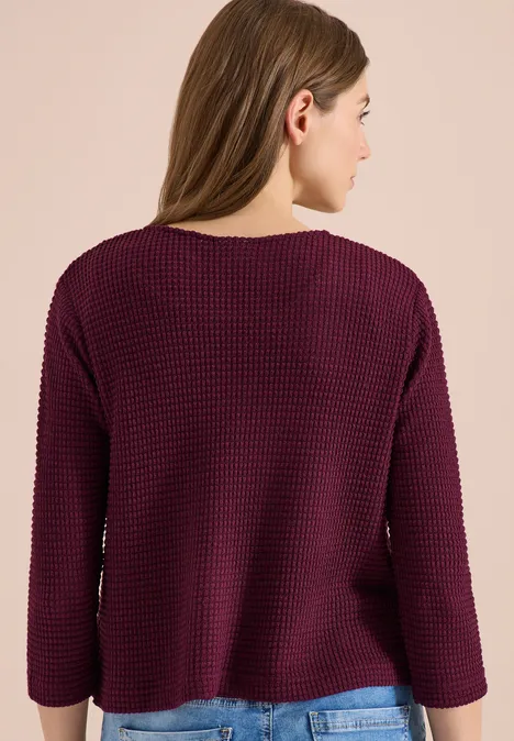 Une personne de dos portant un pull en maille violet foncé et ample.