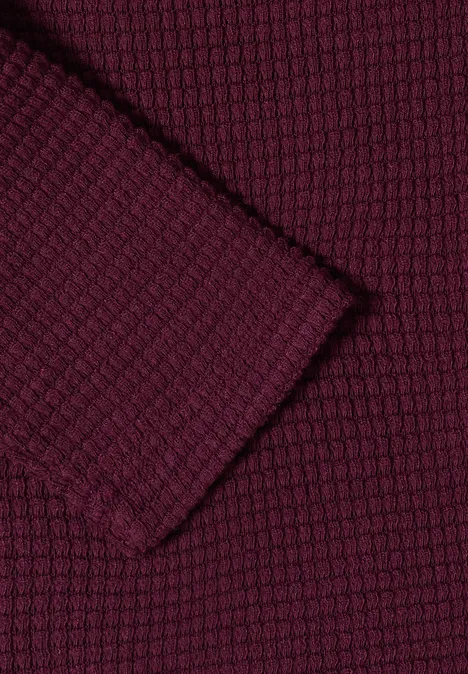 Gros plan d'un tissu tricoté bordeaux à motif nid d'abeille texturé.