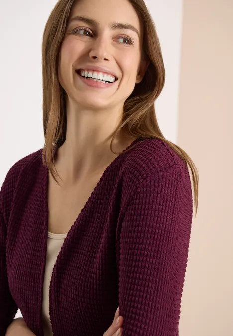 Femme portant un gilet violet sur un débardeur blanc devant un fond neutre