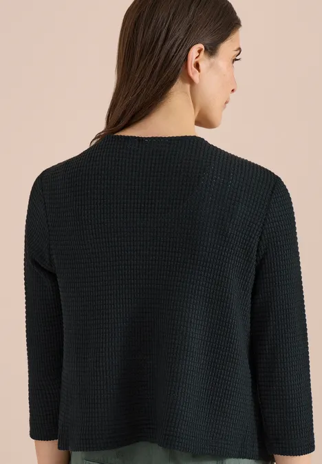 Femme de dos portant un haut en maille noire texturée à manches 3/4.