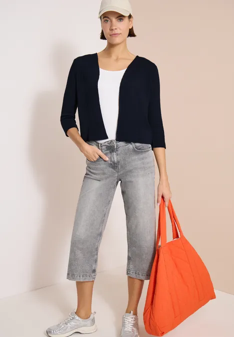 Veste ouverte à manches 3/4 en look ajouré universal blue Femme en gilet bleu marine, débardeur blanc, jean gris court et grand sac fourre-tout orange.