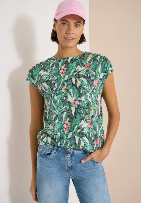 Shirt met burn-out look khaki Een persoon draagt een groen t-shirt met tropisch patroon en een jeans, staand voor een lichte achtergrond.