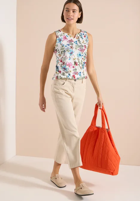 Top mit Split Neck und Raffung light alabaster white Frau in geblümtem Top, hellen Cropped-Hosen und Mokassins trägt große rote Tasche vor neutralem Hintergrund.