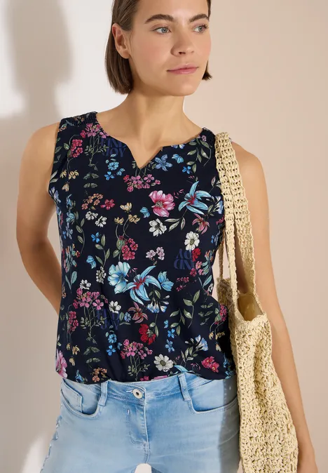 Femme portant un haut sans manches bleu foncé à imprimé fleuri coloré et un sac en paille.