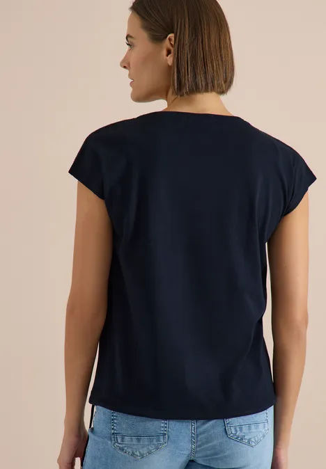 Rückansicht einer Person mit dunkelblauem T-Shirt und hellen Jeans, kurze Haare.