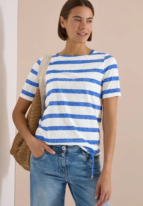 Femme porte un t-shirt rayé bleu et blanc, un jean et un sac en paille sur l'épaule.