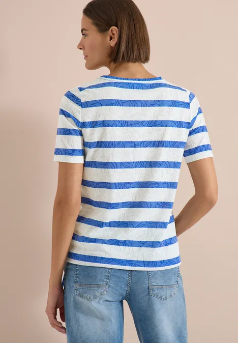 Personne vue de dos portant un t-shirt blanc à rayures bleues et un jean.