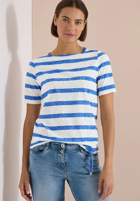 Personne devant un mur clair, vêtue d'un t-shirt rayé bleu et blanc et d'un jean bleu.