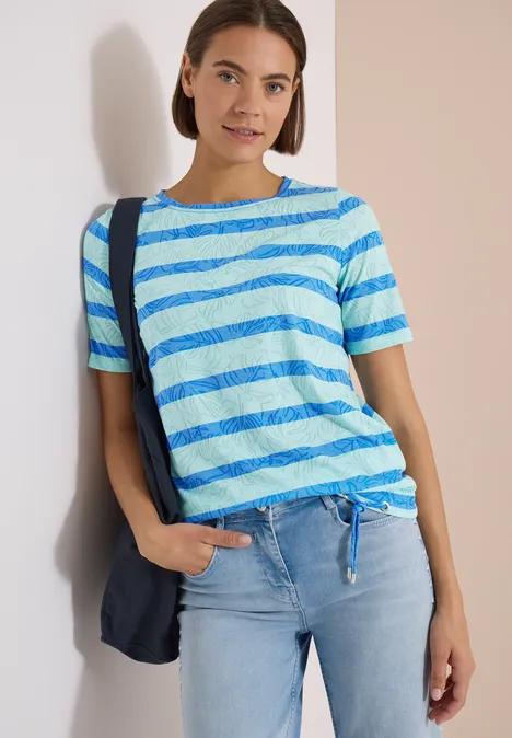 Femme en t-shirt rayé bleu clair et blanc noué, jean et un sac à bandoulière bleu marine.