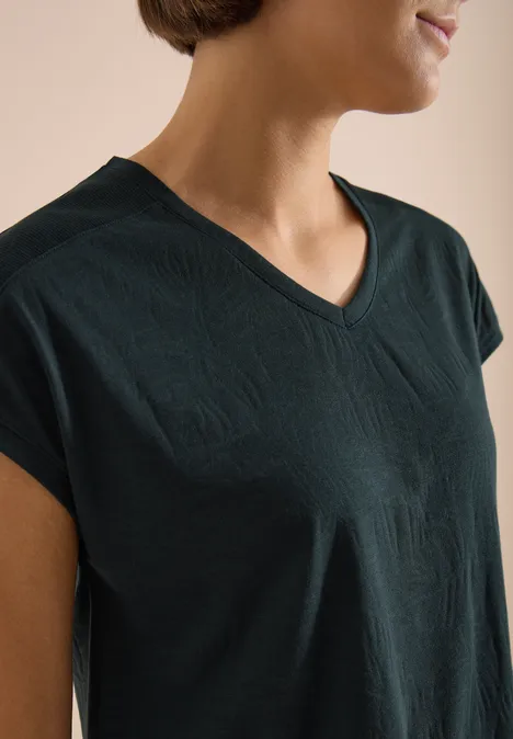 Frau trägt dunkelgrünes V-Ausschnitt-T-Shirt, Oberkörper seitlich zu sehen.