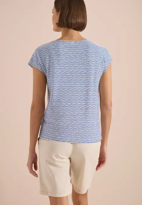 Personne vue de dos portant un t-shirt bleu-blanc rayé et un short beige sur un fond neutre.