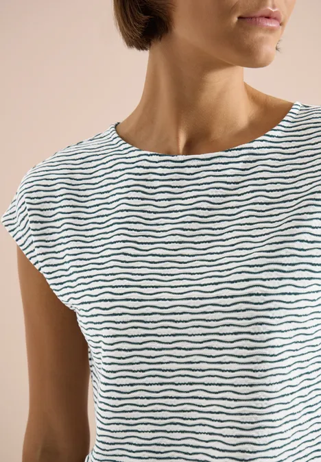 Plan rapproché d'une femme en t-shirt blanc simple à fines rayures ondulées noires.