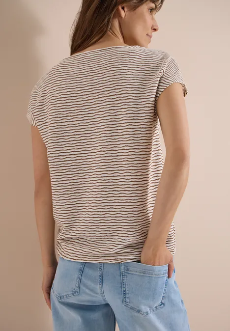 Vrouw van achteren in gestreept T-shirt en spijkerbroek, handen in de zakken.
