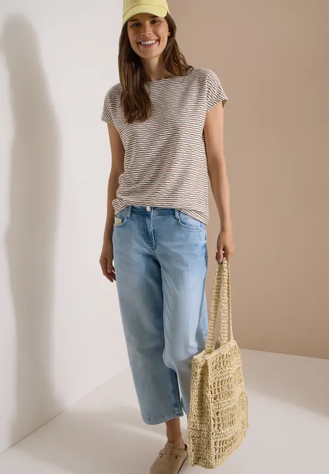 Vrouw in gestreept shirt, wijde spijkerbroek en gevlochten rieten tas.