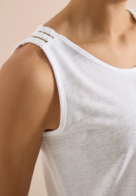 Ein Oberkörper in einem weißen Tanktop mit drei schmalen Trägern.