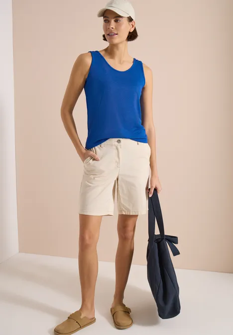 Person trägt blaue ärmellose Bluse, beige Shorts und hält eine dunkelblaue Tasche.