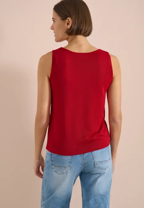 Top avec col en V arrondi et détail tressé tamarillo red Femme de dos portant un débardeur rouge et un jean bleu clair sur fond uni.