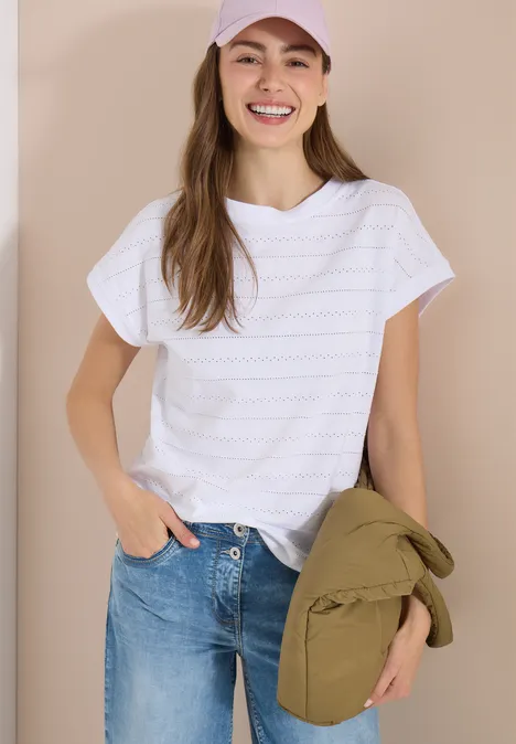 T-shirt structuré avec col bateau White Frau in weißem T-Shirt und blauen Jeans, hält grüne Jacke, vor neutralem Hintergrund.