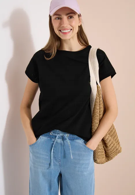 T-shirt structuré avec col bateau Black Frau in schwarzem T-Shirt und Jeans mit Stroh-Tasche über der Schulter.