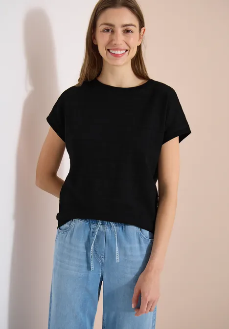 T-shirt structuré avec col bateau Black Person trägt einfaches schwarzes T-Shirt und lockere hellblaue Hosen vor neutralem Hintergrund.
