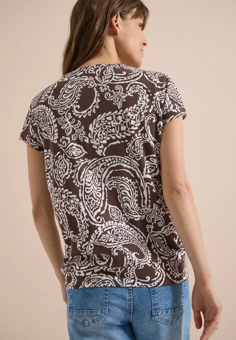 Shirt met V-hals en print brown cacao Vrouw van achteren in een bruin-wit paisley T-shirt en een blauwe spijkerbroek.