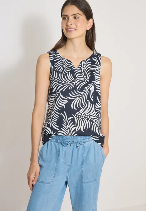 Femme porte un débardeur bleu marine à motifs de feuilles blanches et un pantalon en jean clair.