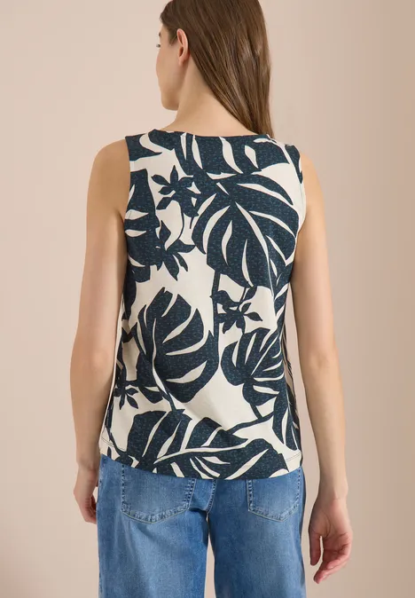 Rückansicht einer Frau mit ärmellosem Top mit großem dunkelblauem Blattmuster und Jeans.