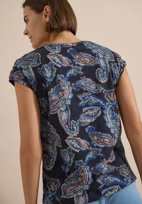 Kurzarm Shirt mit Boat Neck und Raffung universal blue Frau von hinten trägt dunkelblaues T-Shirt mit mehrfarbigem Paisley-Muster, beiger Hintergrund.