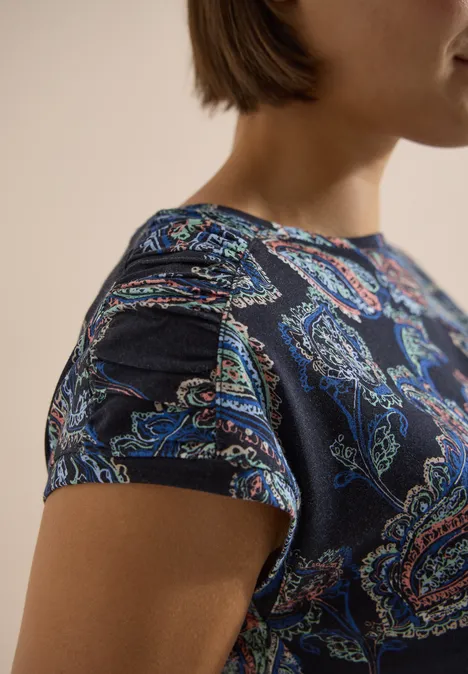 Kurzarm Shirt mit Boat Neck und Raffung universal blue Eine Person trägt ein dunkelblaues T-Shirt mit buntem Paisley-Muster und kurzem Ärmel.