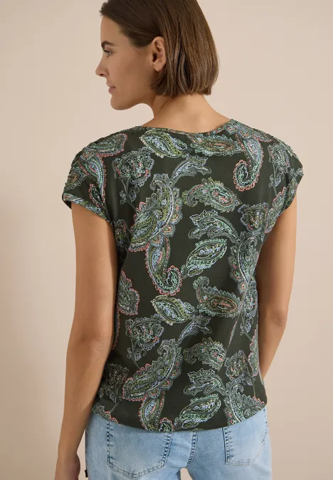 Frau von hinten in dunkelgrünem Paisley-Shirt und hellblauen Jeans.