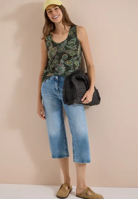 Frau mit unkenntlichem Gesicht in gemustertem Top, Cropped-Jeans und Sandalen mit Strohtasche.