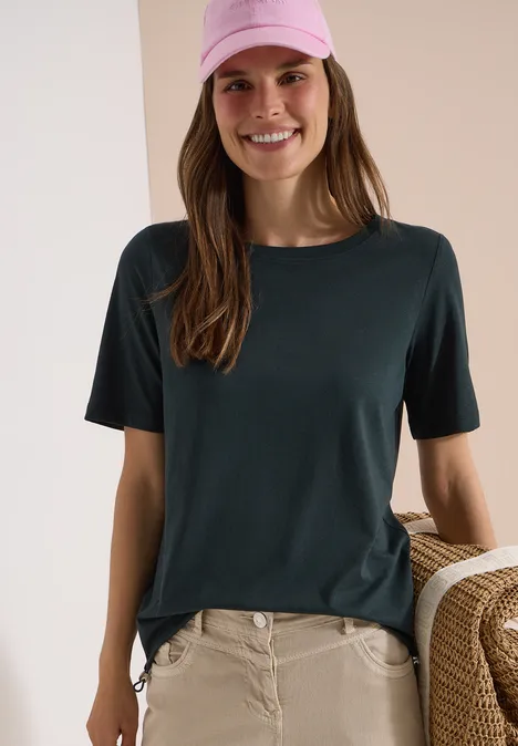 Vrouw met donkergroen T-shirt, beige broek en rieten tas