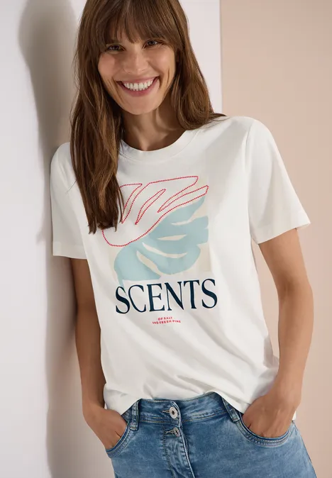 Wit T-shirt met ‘SCENTS’-opdruk en roze-blauw grafisch motief, gecombineerd met een jeans.