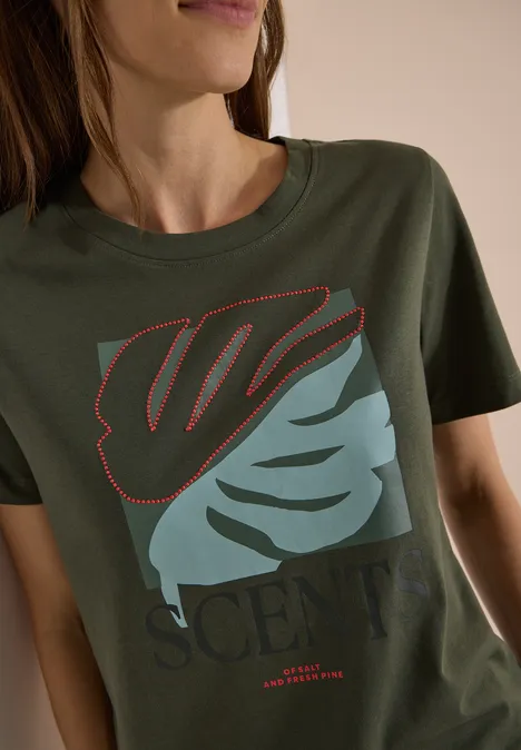 Olijfgroen T-shirt met gestileerd, tweekleurig blad en de tekst 'SCENT', gedragen door vrouw.