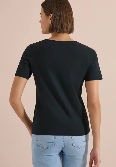 Femme de dos portant un t-shirt noir à manches courtes et un jean bleu clair sur fond neutre.