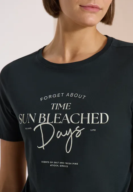 Femme portant un T-shirt noir avec l'inscription blanche 'Forget about time sun bleached days'.