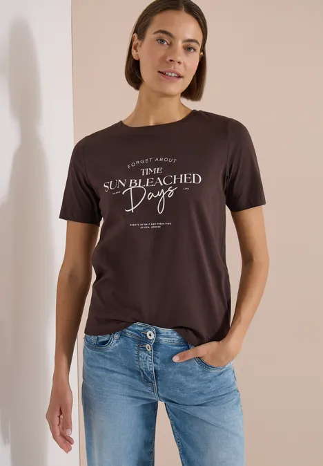Eine Person trägt ein dunkelgraues T-Shirt mit weißem Schriftzug 'The sun bleached days' und blaue Jeans.