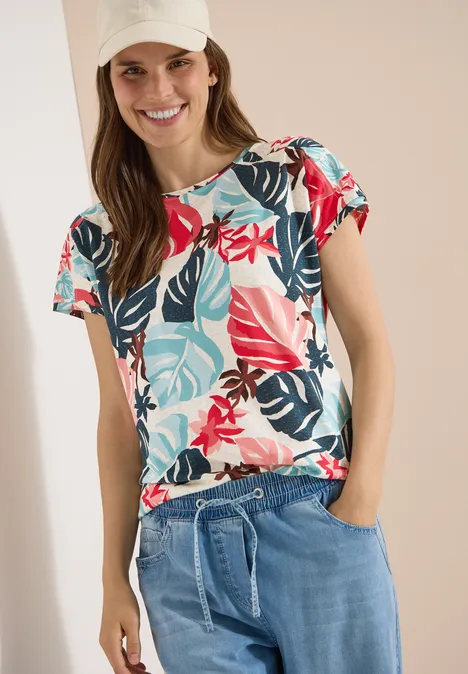 Frau trägt buntes T-Shirt mit tropischem Blumenmuster und leichte Jeanshose mit Kordelzug.