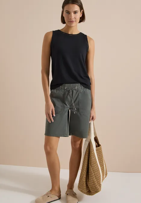 Top mit U-Boot-Ausschnitt und Spitzendetails Black Frau in ärmellosem schwarzen Top, grauen Shorts und Sandalen, trägt eine geflochtene Strandtasche.