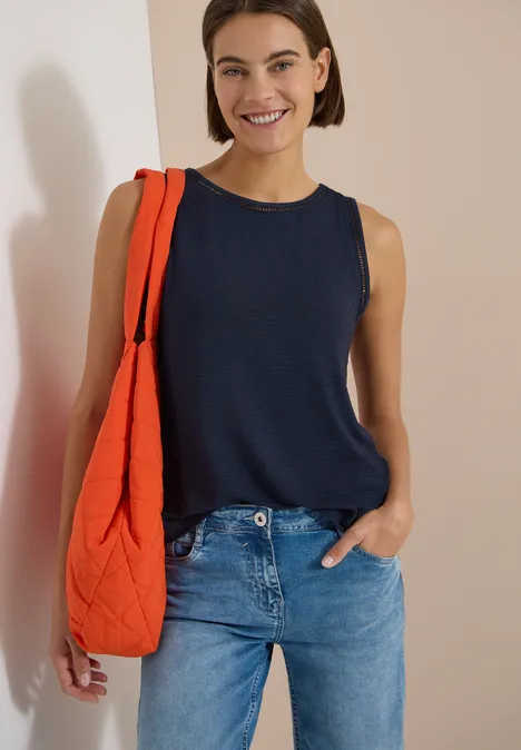 Frau trägt dunkelblaues ärmelloses Top, Jeans und eine orange gesteppte Umhängetasche.