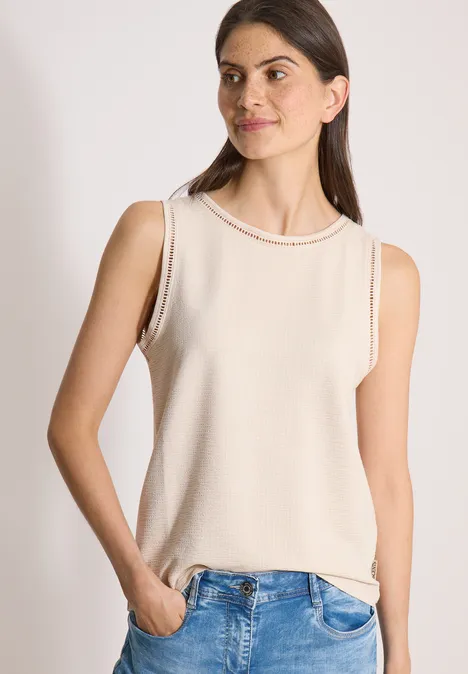 Top mit U-Boot-Ausschnitt und Spitzendetails pearl beige Frau mit ärmellosem beigem Oberteil und Jeans vor hellem Hintergrund.