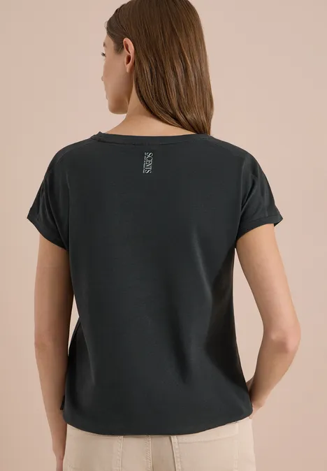 T-Shirt mit Rundhals und Embroidery palm breeze green Eine Frau von hinten trägt ein schwarzes T-Shirt mit kurzen Ärmelumschlägen und eine beige Hose vor hellem Hintergrund.