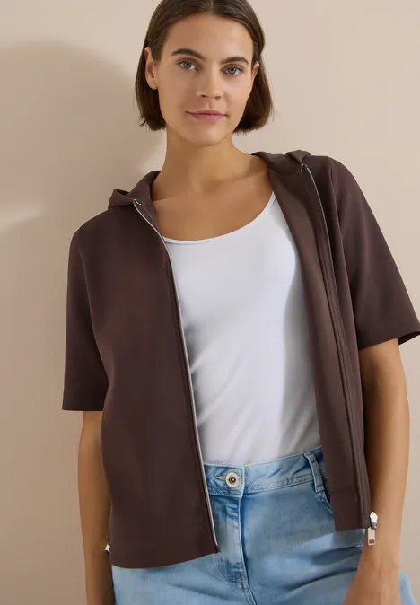 Kapuzenjacke mit seitlcihen Tunnelzügen brown cacao Person trägt braunen kurzärmligen Kapuzen-Sweatshirt mit Reißverschluss, weißen Tanktop und Jeans.