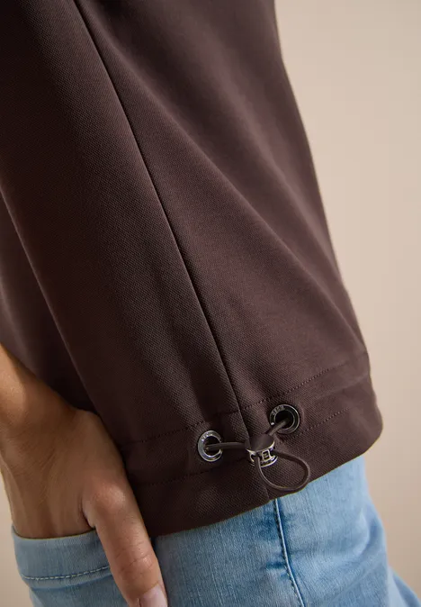 Kapuzenjacke mit seitlcihen Tunnelzügen brown cacao Braunes Oberteil mit Kordelzug am Saum, Hand steckt locker in blauer Jeans.